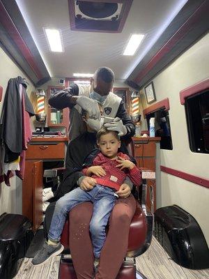 My son getting his haircut from Anthony while sitting in Mama's lap