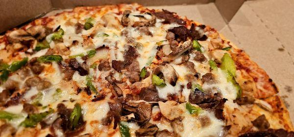 A thin crust pizza with beef, chicken, onions, peppers, and mushrooms covered in cheese.