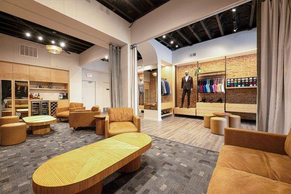 A room with leather chairs and wooden coffee tables by racks of suit and tuxedo pieces and mannequins showcasing a suit or tuxedo for rent.