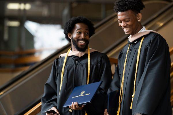 Two graduates celebrate their achievements with diplomas in hand at a Bryant & Stratton commencement ceremony.