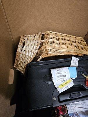 A large suitcase wedged into wicker baskets in unmarked box