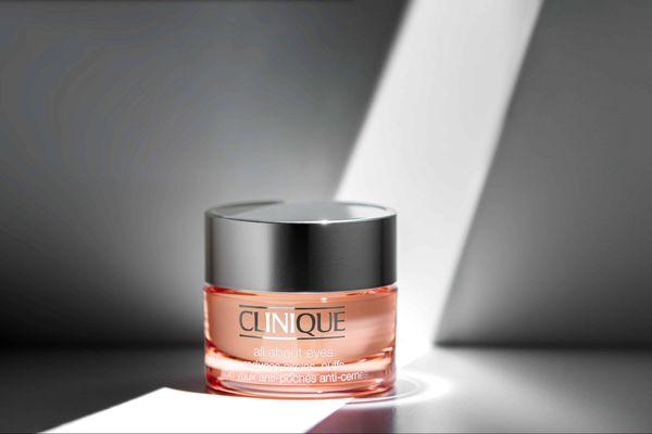 A Clinique All About Eyes cream jar illuminated by dramatic hard light, emphasizing the sleek silver cap and luxurious peach-toned formula.