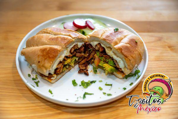 Torta Al Pastor stacked with tender, marinated pork straight off the trompo, caramelized pineapple, creamy avocado, fresh cilantro, & more