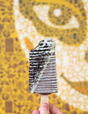 Chocolate Fudgy Brownie Paleta dipped in White Chocolate, topped with Oreo Cookie Crumbs, and drizzled with White Chocolate