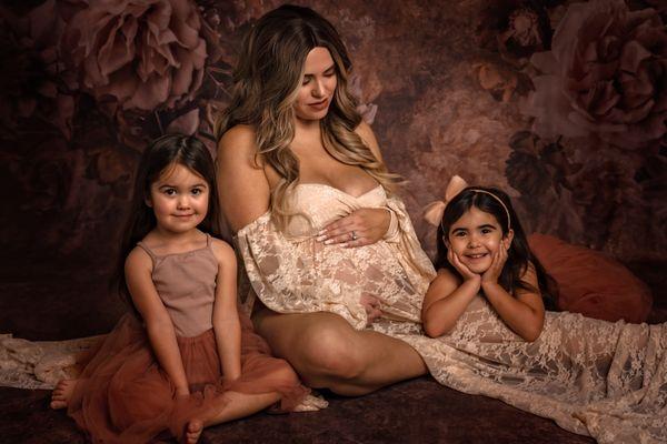 Pregnant woman in pink lace dress sitting with her daughters.