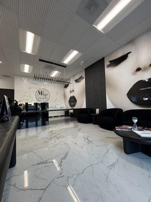 Modern, luxe reception with marble floors, bold wall art & sleek black seating--where your beauty journey begins in style.