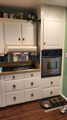 The original kitchen with small wall oven, cooktop range and mirror backsplash. Additionally, the cabinets were not well painted originally.