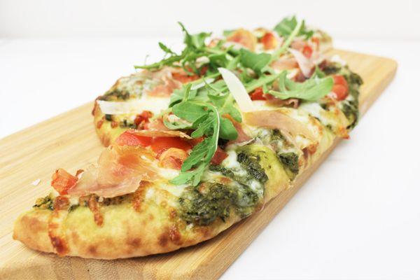 Pesto Prosciutto Flatbread - Sliced prosciutto with tomato and basil pesto sauce topped with mozzarella, arugula, and a dash of lemon