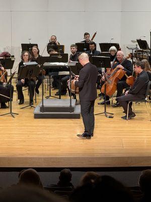 The conductor getting ready to school the audience on the background of the piece they're about to play