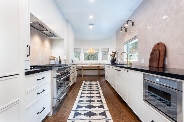 Sleek galley kitchen with white cabinets, black countertops, wood floors, and a bright window. stylish + modern + functional.