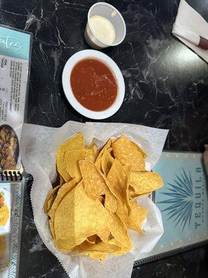 Chips and salsa and a cup of a white sauce.