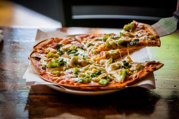 VEGGIE PIZZA with marinara sauce, garlic, cream cheese, green peppers, sun-dried tomatoes, red onions, chopped romaine, and mozzarella.