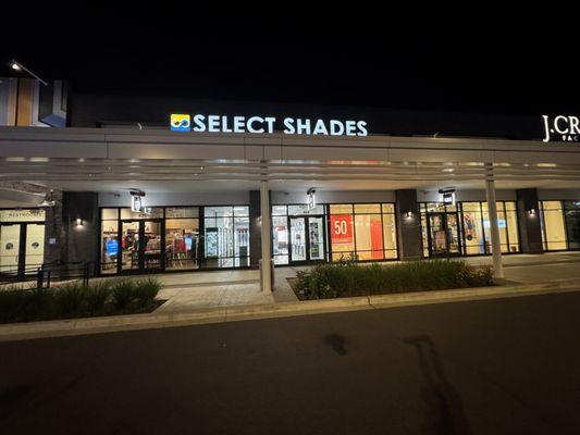 A nighttime view of the outside of Select Shades Sunglass Outlet at Tanger Outlets in Nashville, TN.