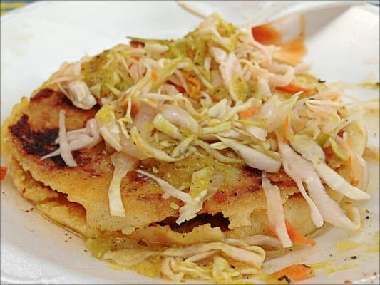 A pupusa with slaw and hot sauce on top. Delicious!