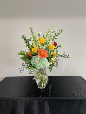 Or. Blue hydrangeas, yellow roses, orange roses burgundy carnations, yellow snapdragons and greenery