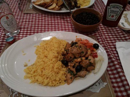 Half order mixed picadinho (pork cubes, shrimp, chourico in garlic and parsley sauce) with yellow rice and black beans in the bowl..