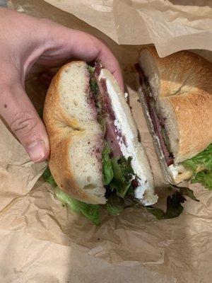 Goat cheese, house jam, bacon, and greens on a plain bagel.