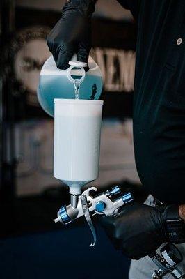 Tech is pouring in botanical solution into handheld disinfecting device prior to misting facility.