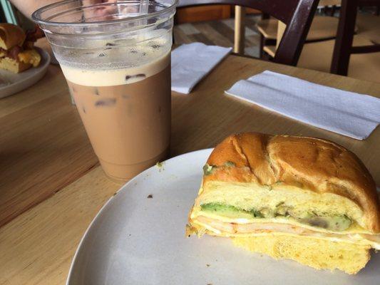 Eggs, avocado and asiago cheese on a roll with and iced latte.